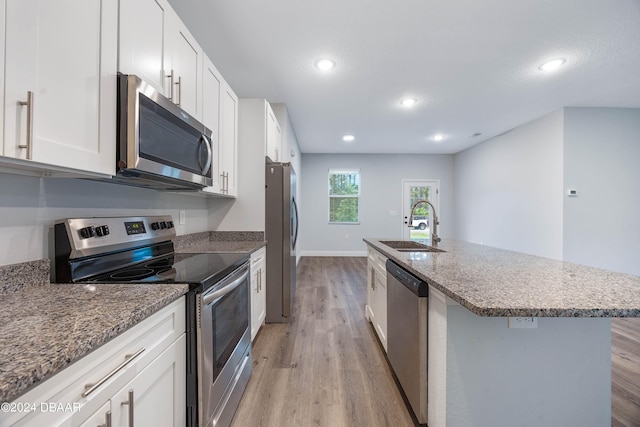 kitchen featuring stainless steel appliances, white cabinetry, sink, an island with sink, and light hardwood / wood-style floors