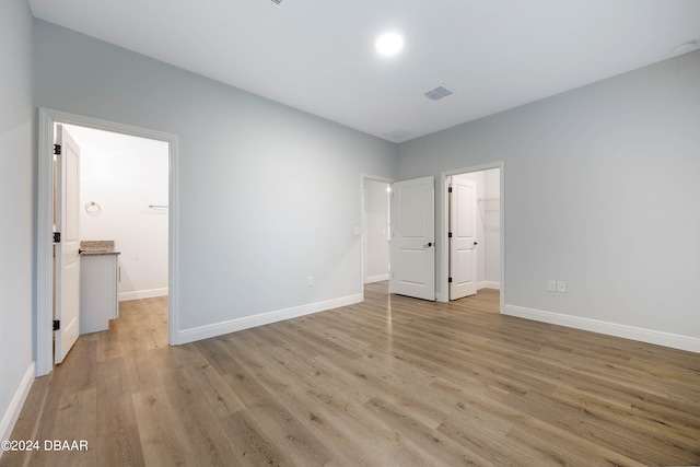 unfurnished bedroom featuring ensuite bathroom, light hardwood / wood-style floors, a walk in closet, and a closet