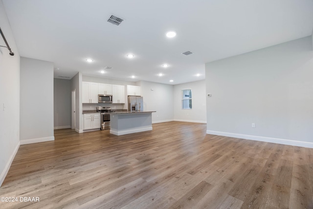 kitchen featuring a kitchen island with sink, white cabinetry, light wood-type flooring, appliances with stainless steel finishes, and dark stone countertops