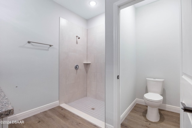 bathroom with hardwood / wood-style floors, tiled shower, and toilet