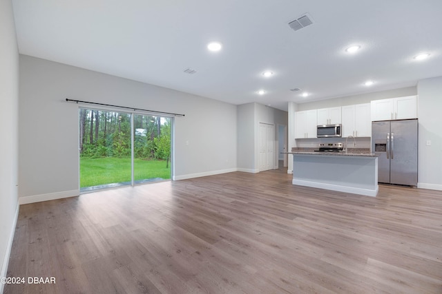 kitchen with white cabinets, a kitchen island with sink, stone countertops, light wood-type flooring, and appliances with stainless steel finishes