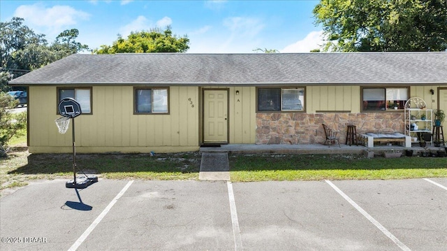 ranch-style house with stone siding, a shingled roof, and uncovered parking