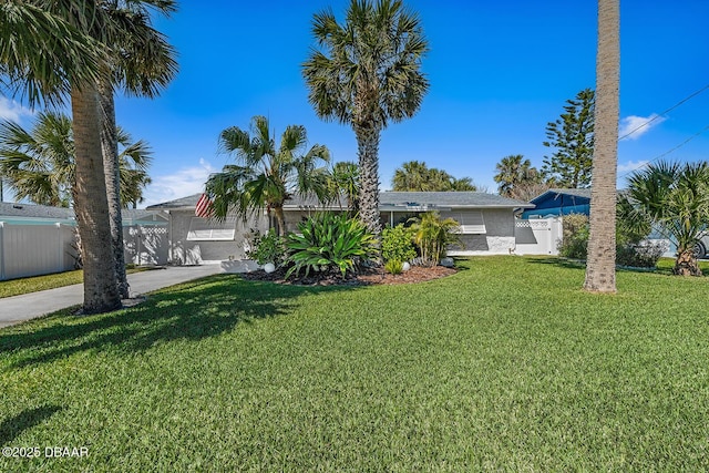 view of front facade featuring stucco siding, concrete driveway, a front lawn, and fence