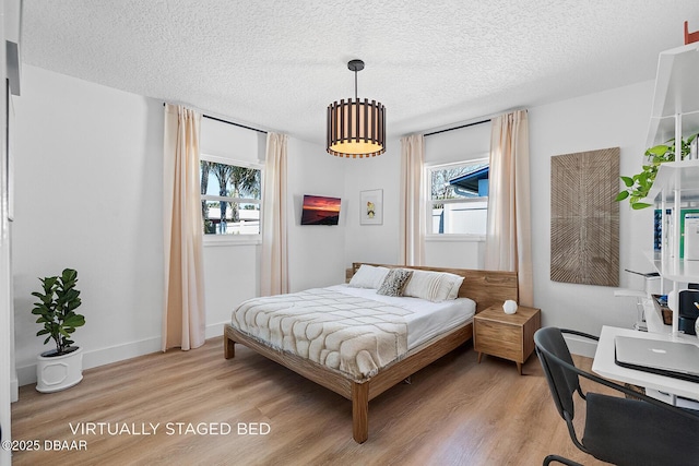 bedroom featuring multiple windows, light wood-style flooring, baseboards, and a textured ceiling