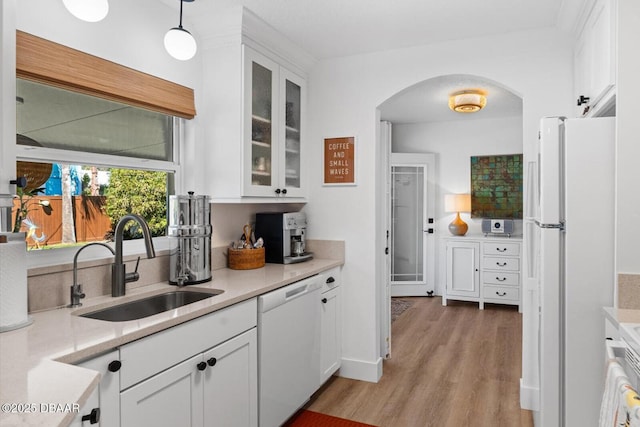 kitchen featuring light countertops, a sink, white appliances, white cabinets, and arched walkways