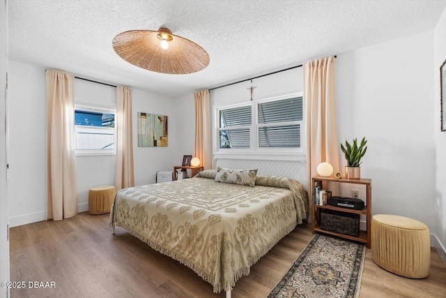 bedroom featuring baseboards, a ceiling fan, wood finished floors, and a textured ceiling