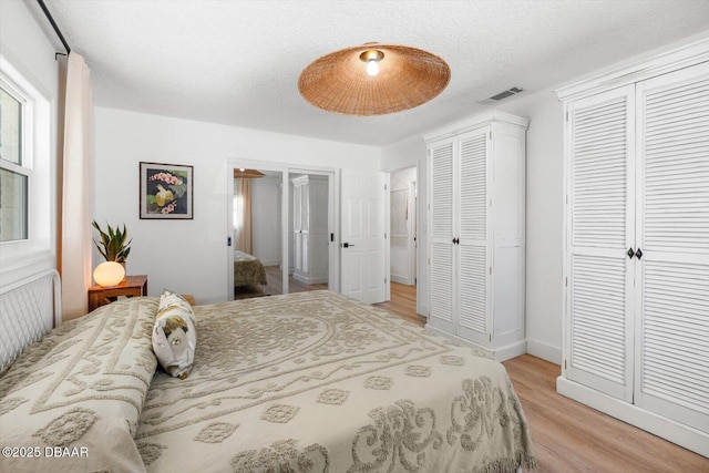 bedroom featuring light wood-style flooring, visible vents, two closets, and a textured ceiling