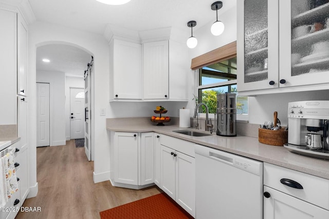 kitchen featuring white cabinetry, light wood-type flooring, a sink, arched walkways, and dishwasher