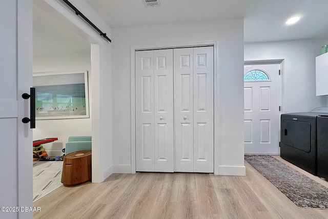 washroom with light wood-style flooring, baseboards, a barn door, and laundry area