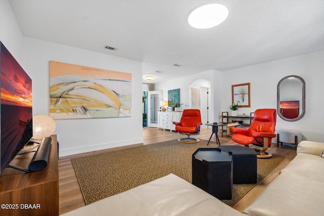 living room with baseboards, visible vents, wood finished floors, and arched walkways