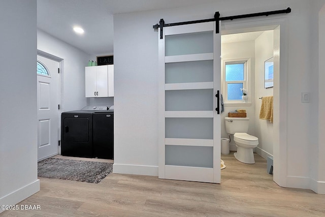 clothes washing area featuring washer and clothes dryer, light wood-type flooring, a barn door, and cabinet space