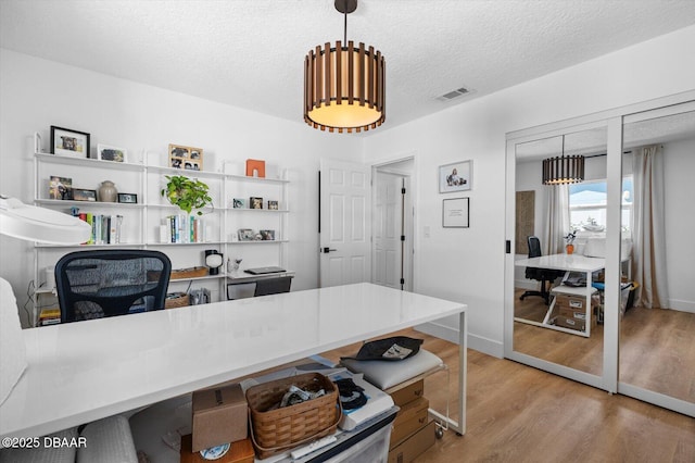 office space featuring a textured ceiling, baseboards, light wood finished floors, and visible vents