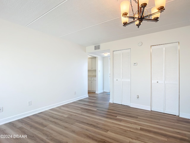 unfurnished bedroom featuring wood-type flooring, a textured ceiling, two closets, and an inviting chandelier