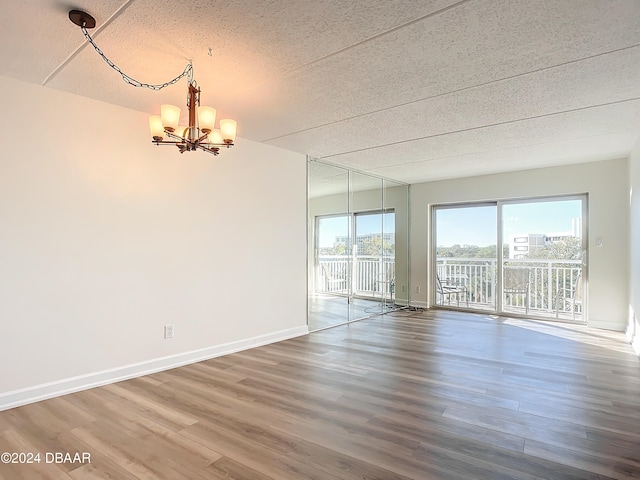 empty room featuring wood-type flooring, a textured ceiling, and an inviting chandelier