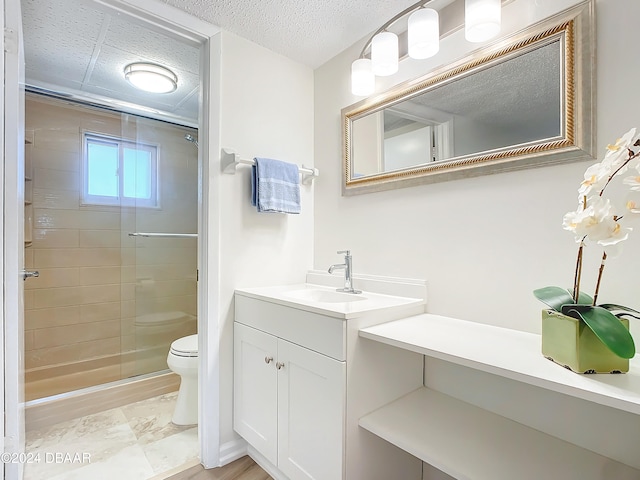 bathroom with a textured ceiling, vanity, toilet, and a shower with shower door