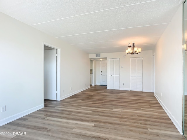 empty room featuring a textured ceiling, light wood-type flooring, and a notable chandelier