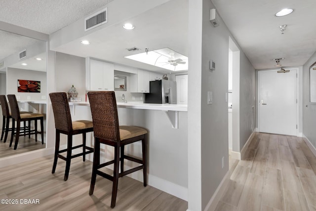 kitchen featuring a breakfast bar, white cabinets, light hardwood / wood-style flooring, stainless steel fridge, and kitchen peninsula