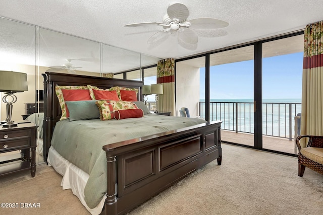 bedroom with access to exterior, ceiling fan, a wall of windows, a textured ceiling, and a water view