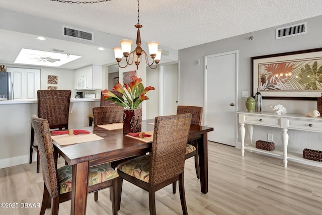 dining area featuring a skylight, an inviting chandelier, a textured ceiling, and light wood-type flooring