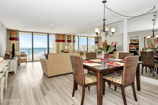 dining space with light wood-type flooring, a textured ceiling, a wall of windows, and a notable chandelier