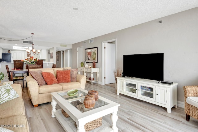 living room featuring a notable chandelier, light wood-type flooring, and a textured ceiling