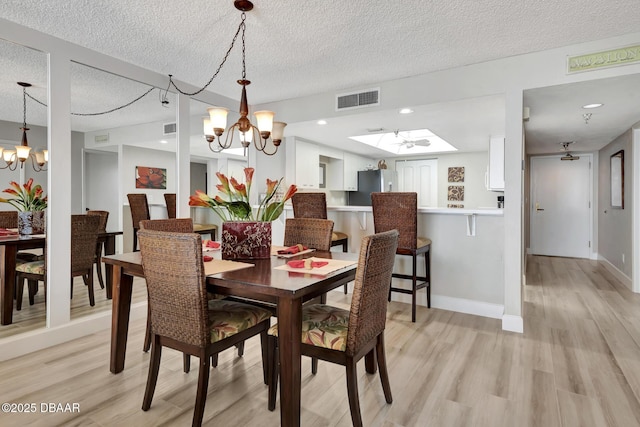 dining area with a chandelier, a textured ceiling, a skylight, and light hardwood / wood-style floors