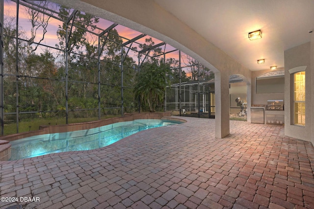 pool at dusk with a lanai, an outdoor kitchen, area for grilling, and a patio area