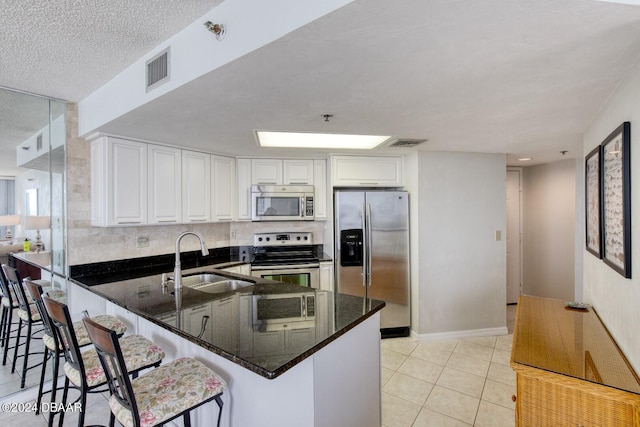 kitchen featuring sink, stainless steel appliances, kitchen peninsula, dark stone countertops, and white cabinets