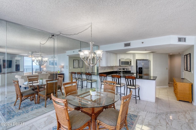 dining area with ceiling fan with notable chandelier and a textured ceiling