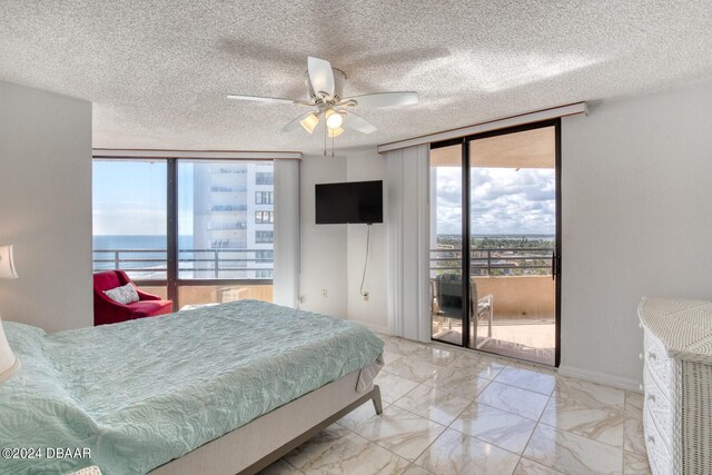 bedroom featuring access to exterior, a textured ceiling, expansive windows, and ceiling fan