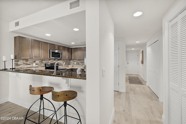 kitchen with a kitchen breakfast bar, kitchen peninsula, stainless steel appliances, and dark stone counters