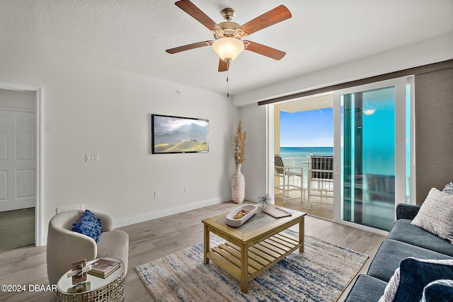 living room with ceiling fan, light hardwood / wood-style floors, a water view, and a textured ceiling