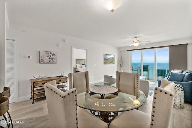 dining area with a water view, light hardwood / wood-style flooring, and ceiling fan