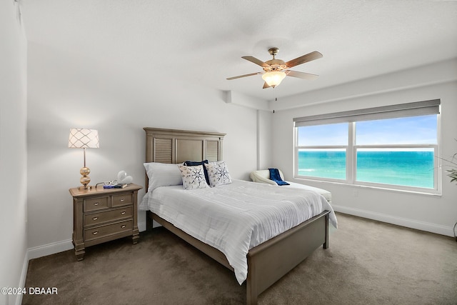 bedroom with ceiling fan, dark carpet, and a water view