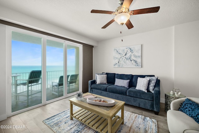 living room featuring hardwood / wood-style flooring, ceiling fan, a water view, and a textured ceiling