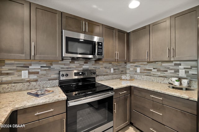 kitchen with backsplash, light stone counters, dark brown cabinetry, and stainless steel appliances