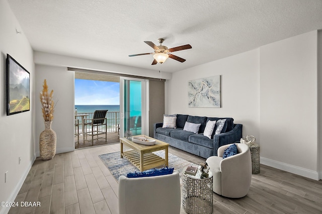 living room with ceiling fan, a water view, light hardwood / wood-style floors, and a textured ceiling