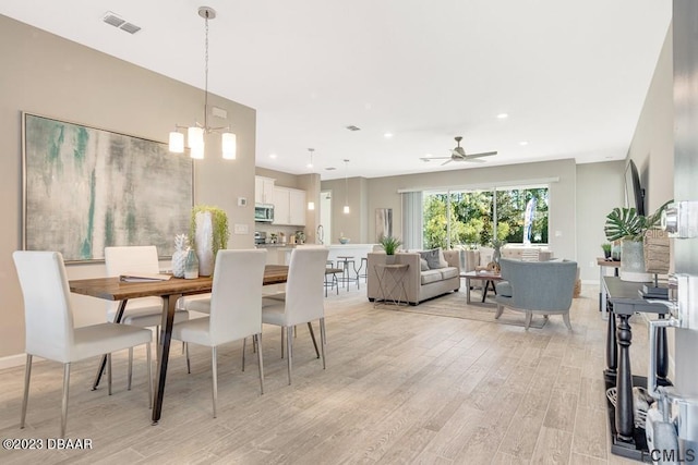 dining room featuring ceiling fan with notable chandelier and light hardwood / wood-style floors