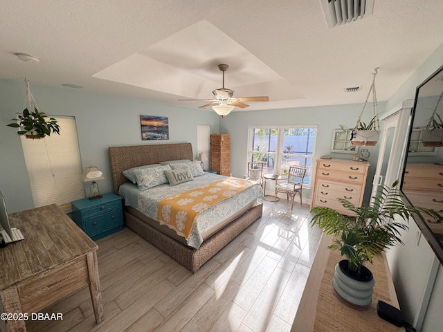 bedroom with ceiling fan, visible vents, a raised ceiling, and wood finished floors