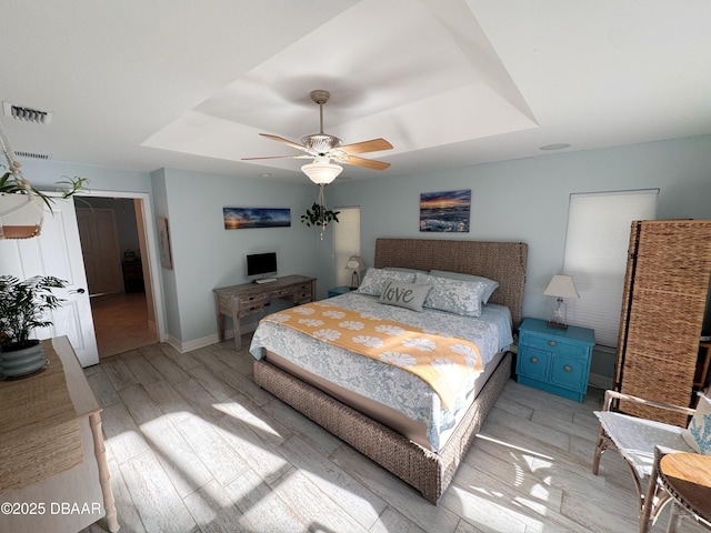 bedroom with a raised ceiling, visible vents, ceiling fan, light wood-type flooring, and baseboards