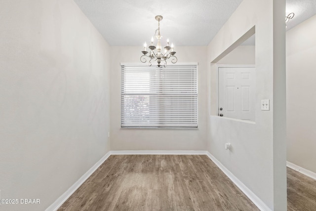 unfurnished dining area featuring a textured ceiling, baseboards, a notable chandelier, and wood finished floors