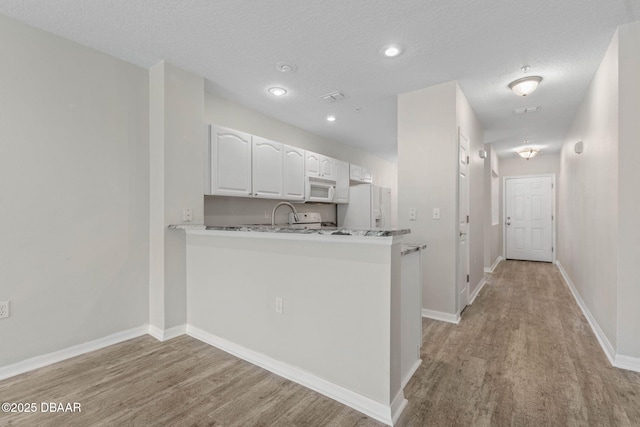 kitchen featuring a peninsula, white appliances, white cabinetry, and light wood-style floors