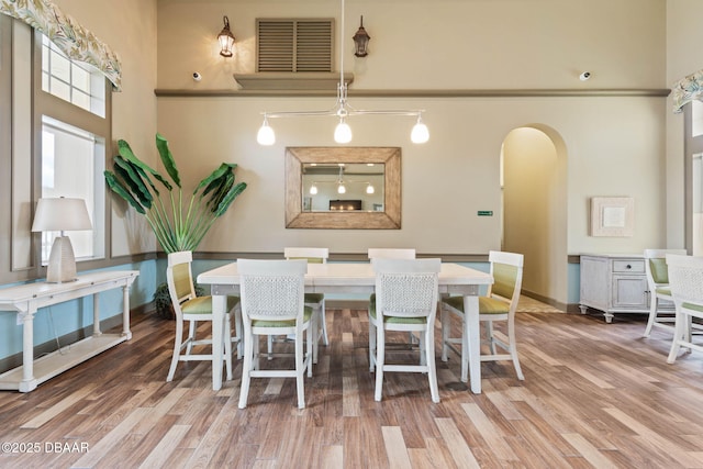 dining area featuring arched walkways, visible vents, a high ceiling, and wood finished floors