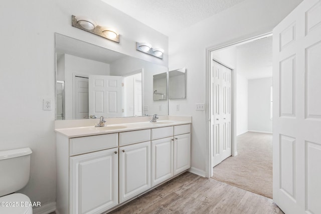 full bathroom with a textured ceiling, double vanity, a sink, and toilet