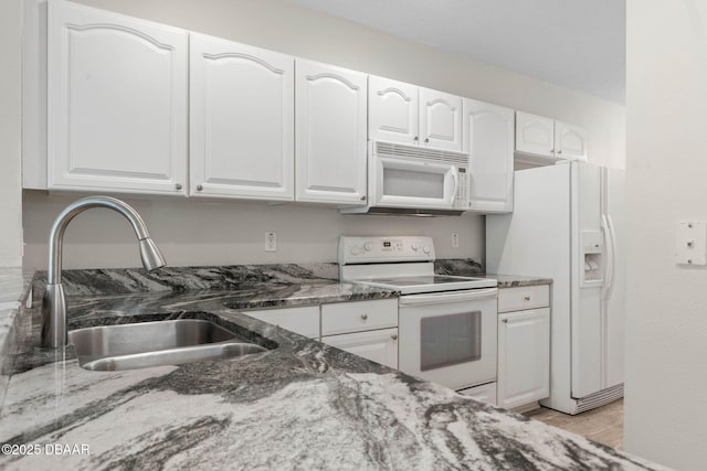 kitchen with white appliances, white cabinetry, dark stone counters, and a sink