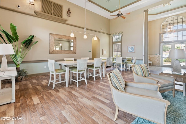 living room with arched walkways, a tray ceiling, wood finished floors, and a towering ceiling