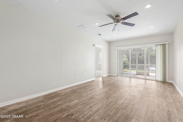 spare room with a textured ceiling, ceiling fan, wood finished floors, visible vents, and baseboards