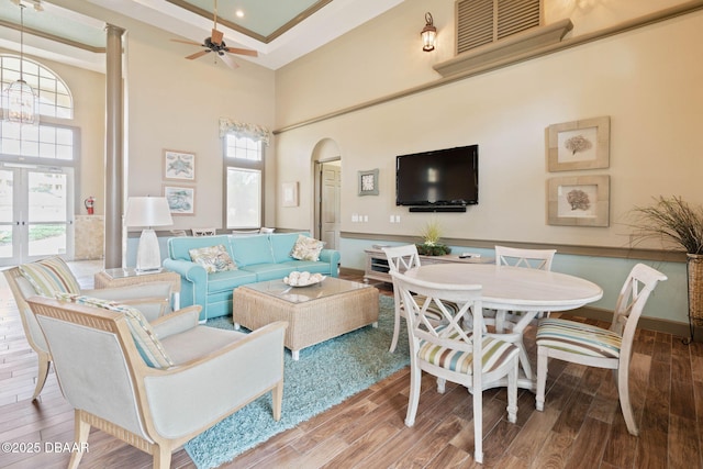 living room with arched walkways, light wood finished floors, ceiling fan with notable chandelier, and a towering ceiling