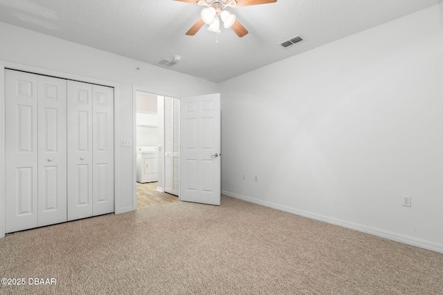 unfurnished bedroom with a closet, light colored carpet, visible vents, a textured ceiling, and washer / dryer