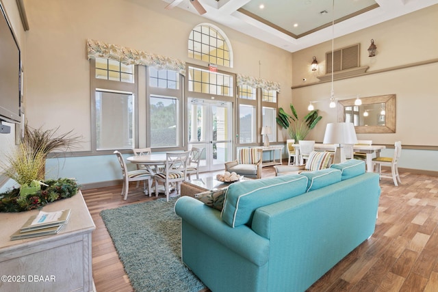 living room featuring wood finished floors, a towering ceiling, visible vents, baseboards, and french doors